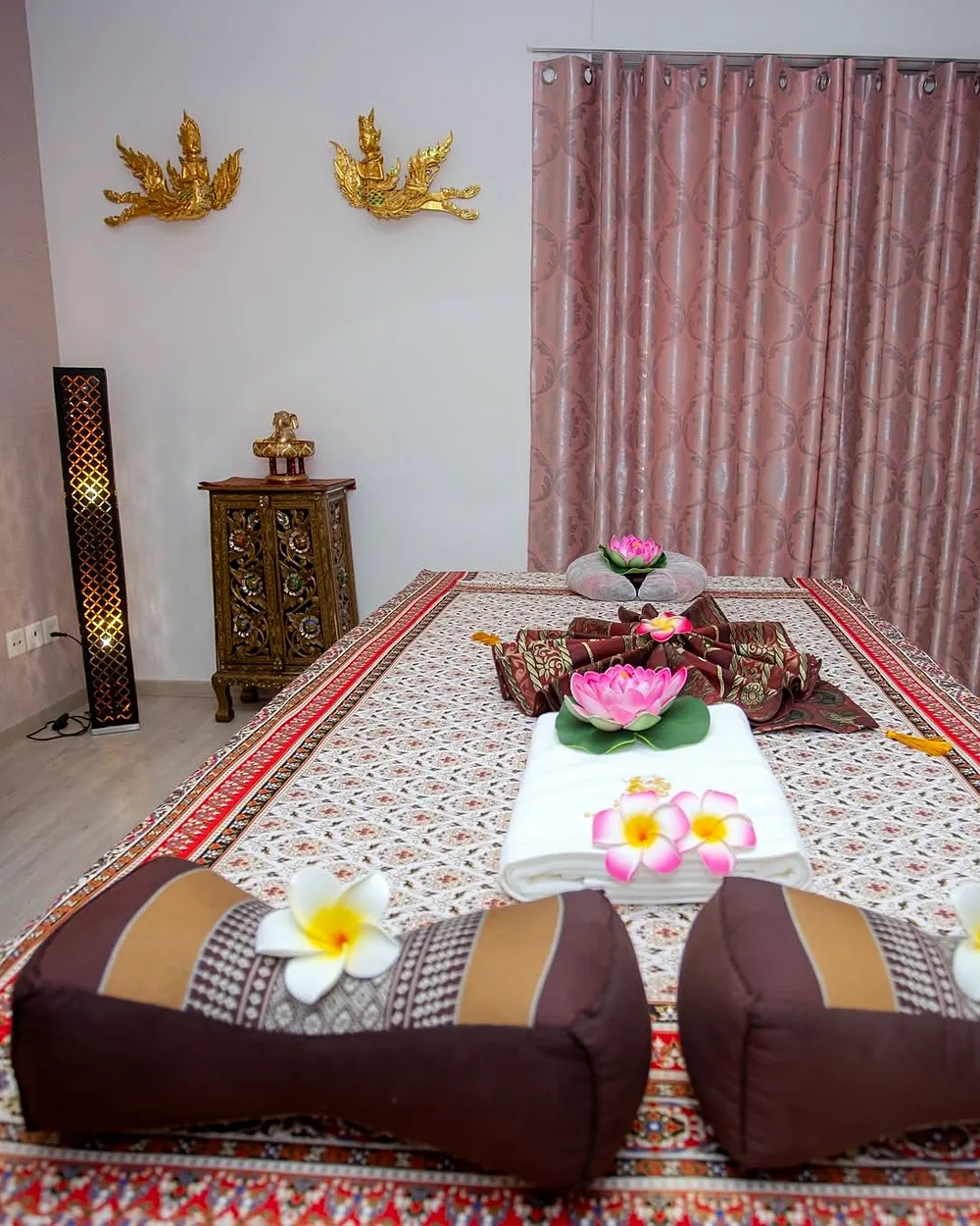 Thai Liege mit Lotusblüten, Frangipani und Kissen, darüber goldene Wandfiguren
